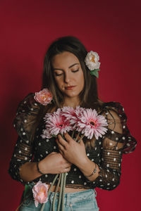Young woman holding flowers while standing against red background