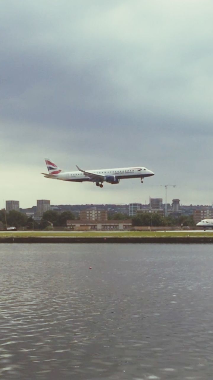 AIRPLANE FLYING OVER RIVER IN CITY