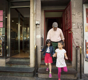 Happy grandfather with grandchildren walking out of store in city