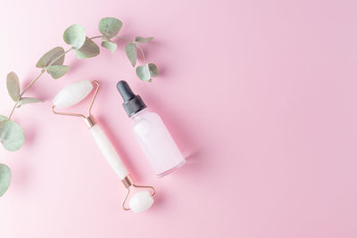 Face massage roller with serum or essential oil bottle on pink background. flat lay, top view