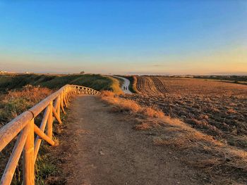 Empty road on field against clear sky during sunset