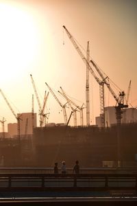 Cranes at construction site against sky during sunset