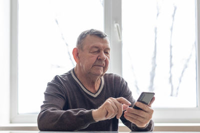 Elderly man dials number in smartphone from home. old senior sends sms on mobile phone