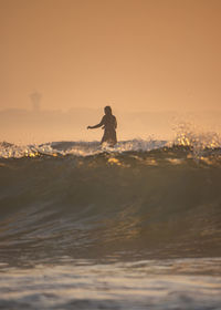 Silhouette woman surfing in sea against sky during sunset