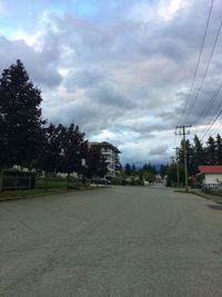 Street by trees against sky in city
