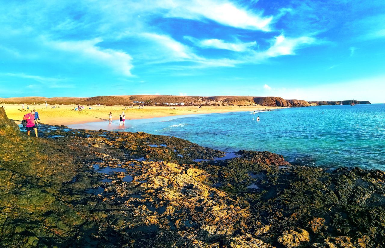 PEOPLE ON BEACH BY ROCKS AGAINST SKY