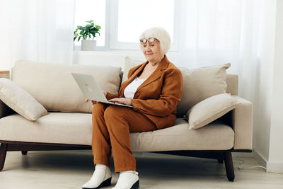 Young woman using laptop while sitting on sofa at home