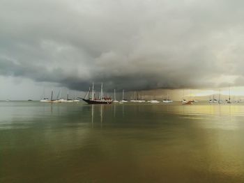 Boats sailing in sea against storm clouds