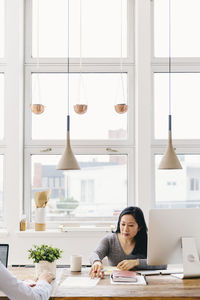 Businesswomen working at desk against windows in office