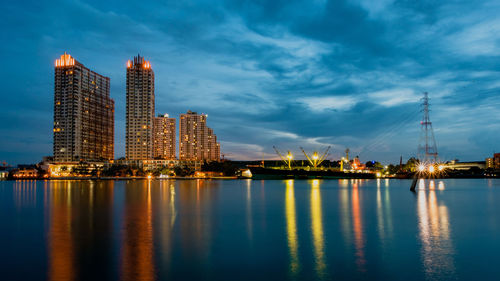 Illuminated buildings by sea against sky