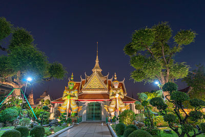 Illuminated temple by building against sky at night