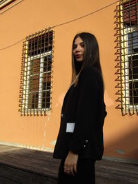 Side view of young woman standing against window