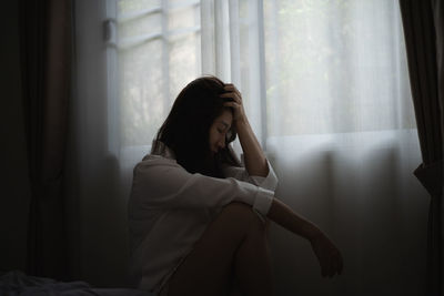 Frustrated woman sitting by window at home