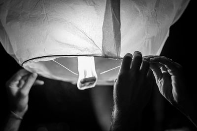 Cropped image of male friends holding lit paper lantern at night