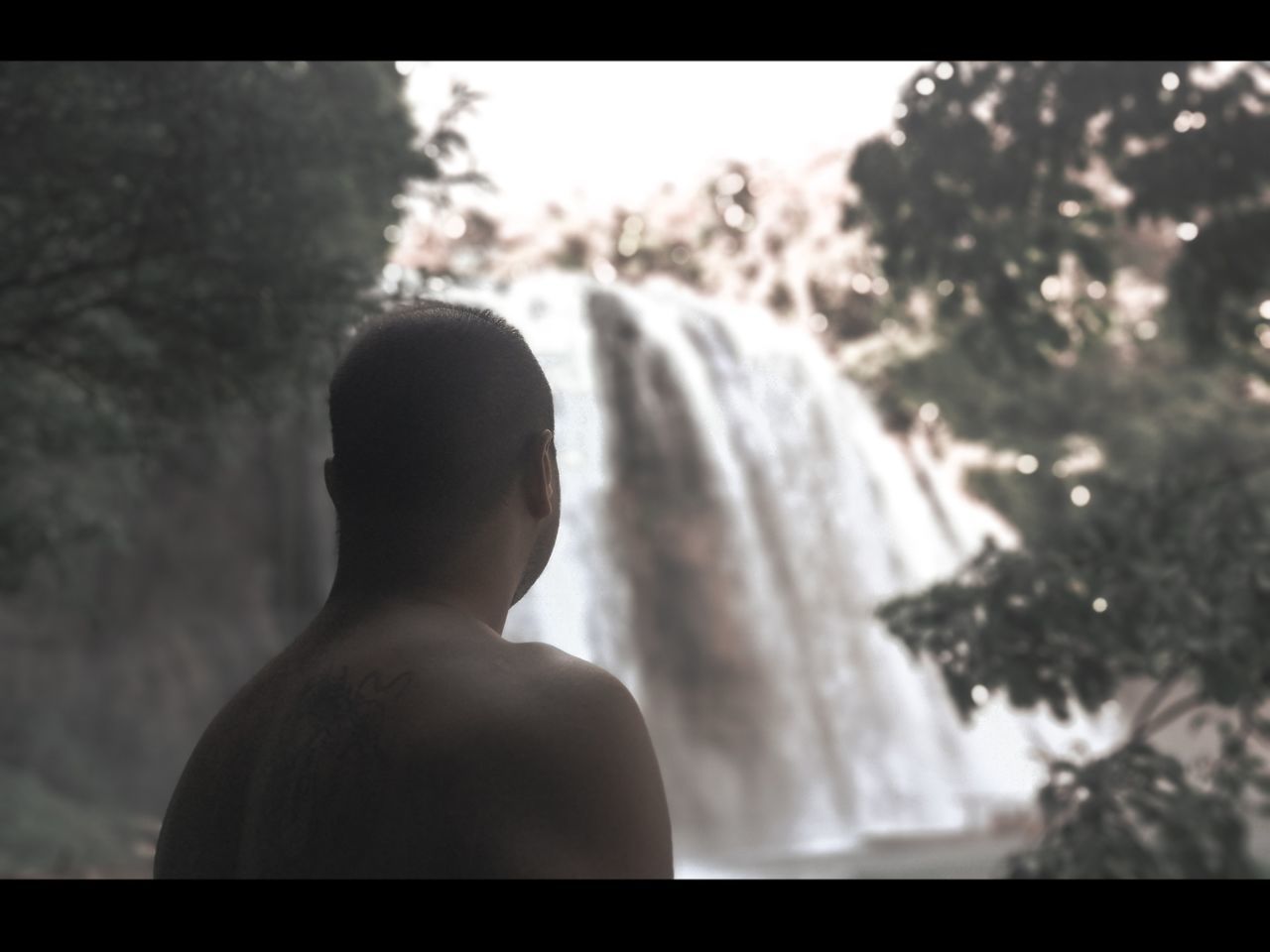 REAR VIEW OF SHIRTLESS MAN LOOKING AT WATERFALL AGAINST SKY