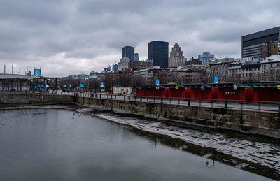 Bridge over river by buildings against sky in city