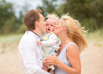 Parents kissing baby girl at beach
