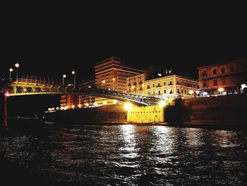 Illuminated city by river against clear sky at night