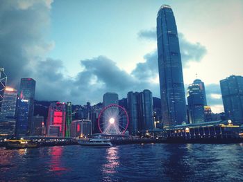 Illuminated city by river against sky