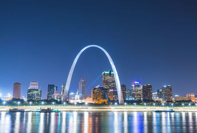 Illuminated city buildings against clear blue sky at night