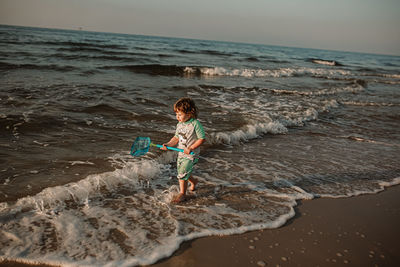 Full length of boy enjoying at beach against sky