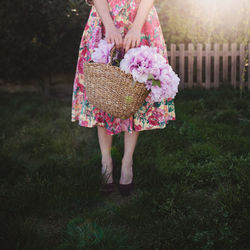 Low section of woman standing in the garden with a basket full of pink flowers