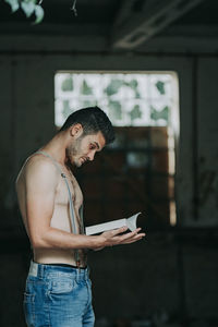 Side view of young man reading book indoors