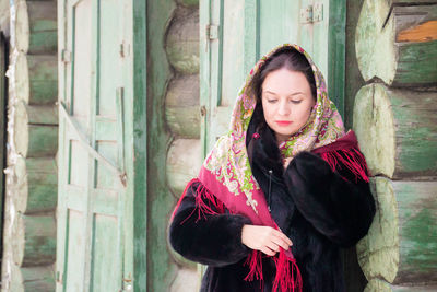 Woman wearing scarf looking away against log cabin