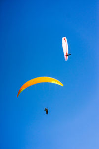 Low angle view of people paragliding against sky