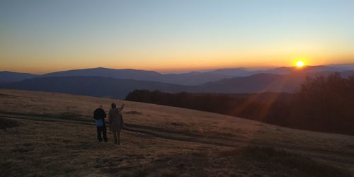 Men standing on landscape against sky during sunset