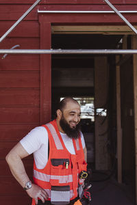 Smiling bearded male construction worker standing with hand on hip at doorway