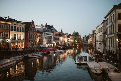 Sailboats moored in canal amidst buildings against sky in city