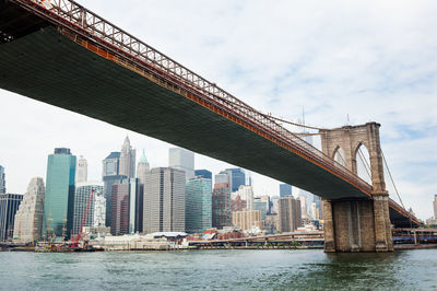 Low angle view of brooklyn bridge over river in city against sky