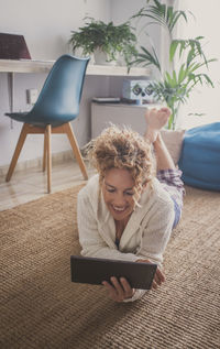 Smiling woman talking on video call lying on floor at home