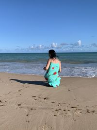 Full length of woman sitting on beach against sky