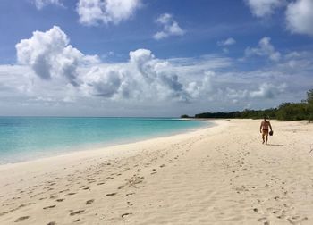 Rear view of woman walking on beach against sky