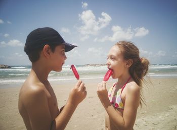 Young couple holding ice cream at beach against sky