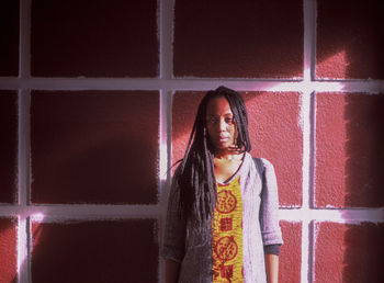 Portrait of young woman with braided hair standing against window