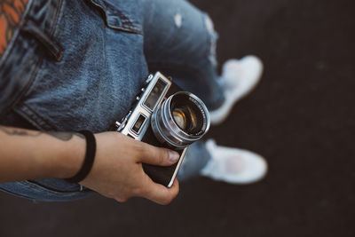 From above crop hands of people in casual wear and white sneakers holding vintage camera on blurred background