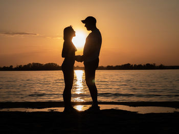 Silhouette couple standing on beach against sky during sunset