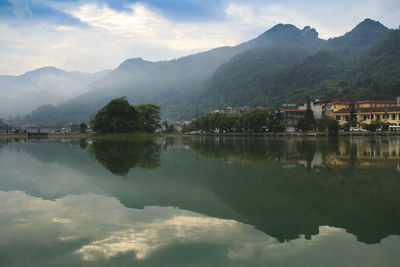Scenic view of lake by buildings and mountains against sky