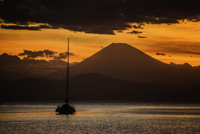 Silhouette sailboat on sea against orange sky