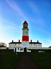 Low angle view of lighthouse by building against blue sky