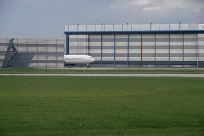 Airplane on runway in front of warehouse on field against sky