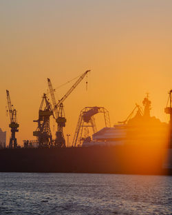 Cranes at commercial dock against sky during sunset