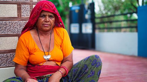 Portrait of indian senior woman sitting near main entrance and looking at camera.