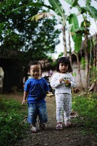 Full length of cute siblings standing against trees