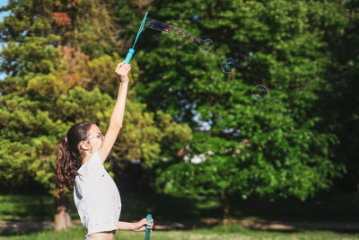 Portrait of a caucasian teenage girl blowing soap bubbles in the park.