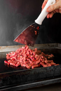 Person holding meat on barbecue grill