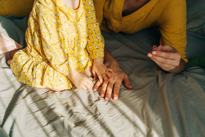 A little daughter paints her mother's nails with polish.